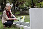Senior woman holding flowers at grave stone