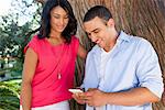 Young couple by tree trunk, man using smartphone