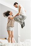 Mid adult couple wearing pyjamas jumping on bed