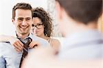 Mid adult woman helping man to fasten tie