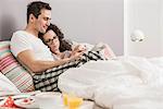 Mid adult couple reading newspaper in bed