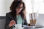 Businesswoman sitting at desk with laptop computer and coffee cup