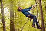 Boy swinging on rope in forest