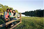 Pre-teen girls sitting on fence, looking at tablet computer and cellphone, outdoors