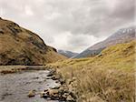 river flows along mountains of barren Scottish countryside with overcast, cloudy skies, Scotland