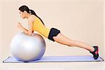Brunette woman doing exercises with fit ball  while isolated on beige background