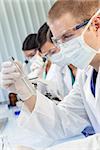 A male medical or scientific researcher or doctor looking at a test tube of clear liquid in a laboratory with female colleagues.