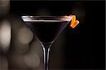 dark cocktail garnished with an orange twist on a dark bar setting