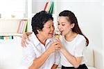 Sharing food. Happy Asian family sharing an ice cream at home. Beautiful senior mother and adult daughter eating dessert together.