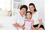 Family generations. Happy Asian family at home, grandparent, parent and grandchild sitting on sofa smiling looking at camera.