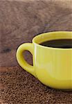 Yellow mug with coffee on the table with a instant coffee granules and wooden board background