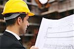 Young man working as engineer in new apartment buildings, looking at building plan in construction site