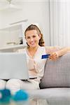 Smiling young housewife with laptop and credit card in living room