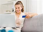 Happy young housewife with laptop and credit card in living room