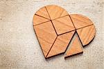 heart version of tangram, a traditional Chinese Puzzle Game made of different wood parts to build abstract figures from them, on white painted barn wood