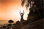 girl silhouette performing yoga on beach during a beautiful sunset