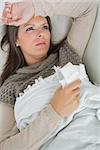 Ill woman lying on sofa with blanket holding a tissue feeling sorry for herself