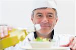 Smiling chef dressing a salad in kitchen