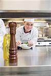 Smiling chef garnishing a salad and looking up in kitchen