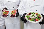 Chef's holding out their salads in kitchen
