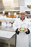 Head chef showing a salad with his team standing behind him