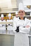 Smiling chef with crossed arms with team standing behnd her