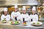 Smiling Chef's standing behind salads in the kithcen