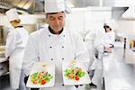 Chef admiring two salmon dishes in his hands in the kitchen