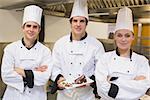 Three Chef's presenting a cake in the kitchen