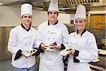 Three Chef's presenting chocolate cakes in the kitchen