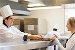 Chef giving a plate to the waitress in the restaurant