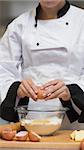 Chef cracking egg into bowl of flour in kitchen