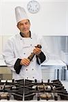 Smiling chef holding a pepper mill at stove