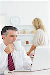 Man drinking coffee while checking laptop in kitchen before work