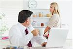 Wife looking disapprovingly at husband using laptop at breakfast in kitchen