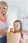 Child looking into grocery bag with mother in kitchen