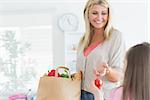 Mother passing tomato to child from paper grocery bag in ktichen