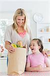 Woman looking into grocery bag beside smiling daughter in the kitchen