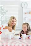 Mother pouring milk into cereal bowl for daughter at breakfast time in kitchen