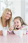 Little girl eating cereal at breakfast with her mother in kitchen