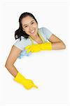 Happy cleaning lady in rubber gloves and apron pointing to white surface