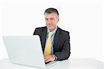 Smiling man writing on his laptop at his desk