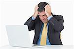 Anxious businessman sitting at his desk with a laptop on a white background