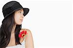 Cheerful woman with flower looking awayon white background wearing a hat