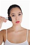 Woman applying powder to face with large makeup brush on white background