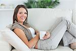 smiling woman lying on the sofa and holding a mug in the living room