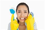 Distressed woman holding cloth and scrubbing brush in apron and rubber gloves