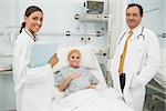 Female and male doctor standing next to a woman patient in a hospital bed