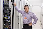 Smiling technician leaning against server in data center