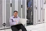 Technician working  with his laptop near the server and sitting on floor of server